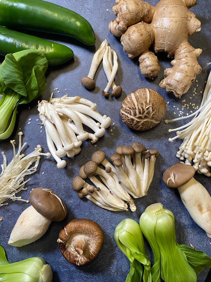 Flat lay of various fresh mushrooms and vegetables on a dark surface, showcasing variety and freshness.